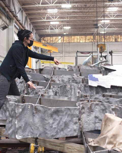 Sarah Sze at the UAP foundry with the steel armature and several of the 130 pieces of polished stainless steel that make up “Fallen Sky.”